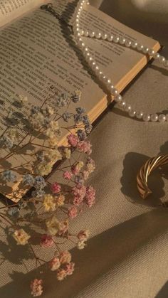 an open book with pearls and flowers on it next to a pair of bracelets