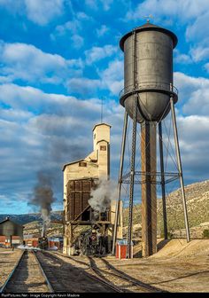 an old water tower with steam coming out of it next to a train track in the desert