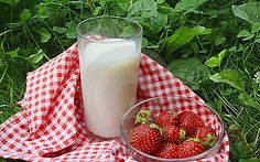 strawberries and milk sitting on a checkered cloth in the grass