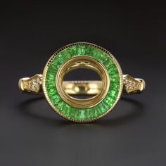 an emerald and diamond ring on a black surface