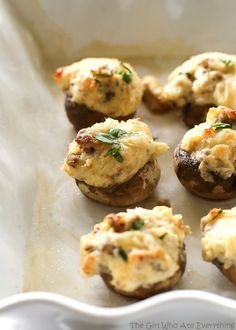 small stuffed mushrooms with cheese and herbs in a white dish on top of parchment paper