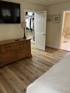 a bedroom with wooden floors and a flat screen tv mounted on the wall above a dresser