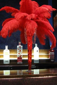 a tall red feathered vase sitting on top of a counter next to liquor bottles