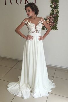 a woman standing in front of a wall with flowers on it and wearing a white dress