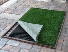 an outdoor area with artificial grass and a drainage grate on the ground in front of it