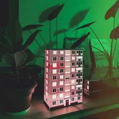 a house model sitting on top of a table next to a potted plant in front of a green wall