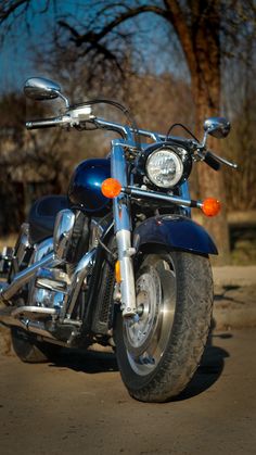 a blue motorcycle is parked on the side of the road in front of some trees