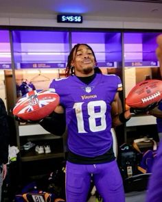 a man holding two footballs while standing in front of a locker room filled with other people