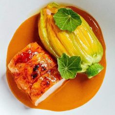 an orange plate topped with meat and vegetables on top of a white tablecloth next to a green leafy plant