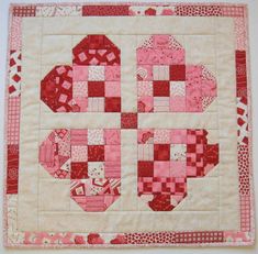 a red and white quilted table topper with pink squares on it's sides