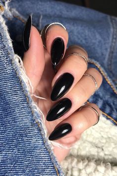 a woman's hand with black nail polish and rings on her fingers, sitting in jeans