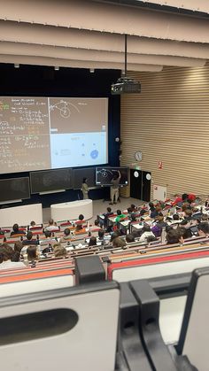 an auditorium full of people sitting at desks in front of a projector screen