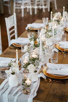 the table is set with white and gold place settings, candles, and greenery