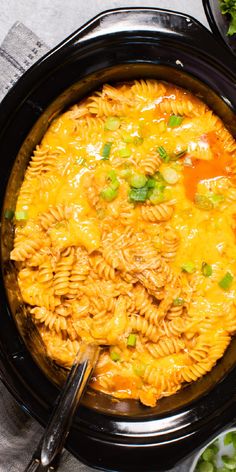 a black bowl filled with pasta and cheese on top of a table next to salad