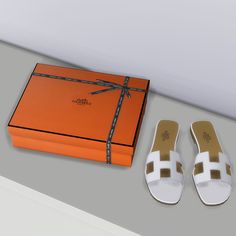 a pair of white shoes next to an orange box with a bow on the top