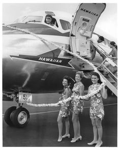 three women standing in front of an airplane with leis around their necks and the door open