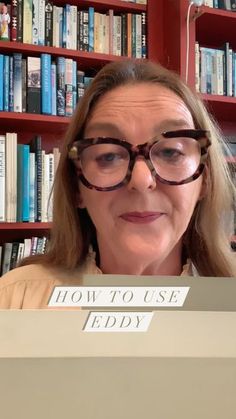 an older woman wearing glasses and reading a book in front of a bookshelf