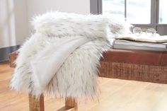 a white fur covered bench in front of a window with glasses on top of it