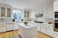 a large kitchen with white cabinets and wood flooring, along with an island in the middle