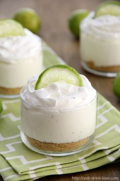 two small desserts with lime and whipped cream in them on a green napkin next to limes