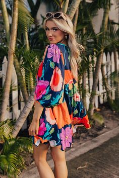 - Embrace floral vibes with this flowy dress! - Soft material with a pink, red, orange, yellow, blue, and green hued floral print - A built-in lining - A v-cut neckline with a tie detail - Long, loose sleeves with elastic cuffs - A lightweight silhouette that ends in a mini dress length hemline Multicolor V-neck Floral Dress With Vibrant Print, V-neck Tropical Print Multicolor Dress, Colorful Floral Print V-neck Dress, Spring Floral V-neck Dress With Vibrant Print, Multicolor Print V-neck Summer Dress, Colorful V-neck Mini Dress, Multicolor Vibrant Print V-neck Dress, Floral Print V-neck Dress For Beach Party, Flowy Tropical V-neck Dress