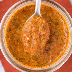 a spoon in a jar filled with soup on top of a red and white checkered tablecloth