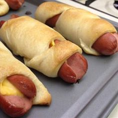 four hotdogs wrapped in bread sitting on top of a pan with buns