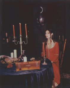 a woman sitting at a table with candles in the middle and an empty box on it