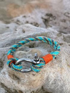 an orange and blue rope bracelet with a metal hook on top of a stone wall