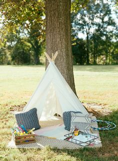 a teepee is set up in the grass near a tree with toys on it