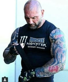 a bald man with tattoos on his arm and wrist holding something in his hand while looking down