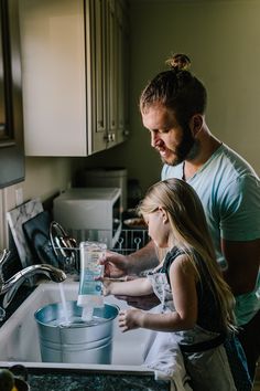 a father and daughter washing dishes in the kitchen sink with their hands on the faucet