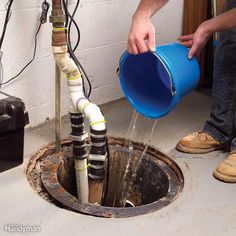 a man is pouring water from a blue bucket into a sewer with multiple pipes running through it