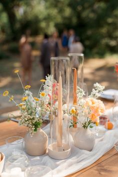 an arrangement of vases and candles on a table with people standing in the background