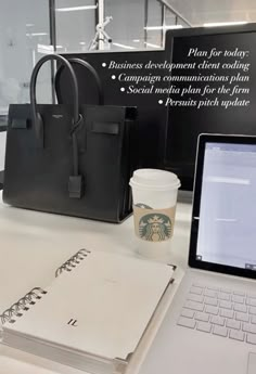 a laptop computer sitting on top of a desk next to a bag and coffee cup