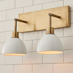 two light fixtures mounted on the wall in a bathroom with white tile and gold accents