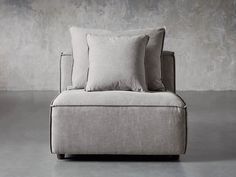 a chair with three pillows on it in front of a cement wall and concrete floor