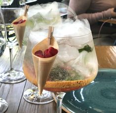 two glasses filled with ice and raspberries sitting on a wooden table next to wine glasses