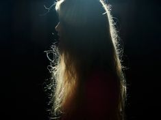 a woman standing in the dark with her head turned to the side and light shining on her