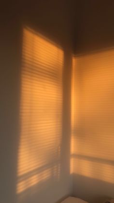 sunlight shining through the blinds in a small room with a bed and night stand next to it