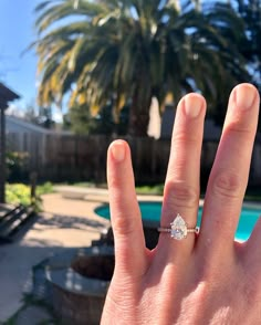 a person's hand with a diamond ring on top of their thumb and palm trees in the background