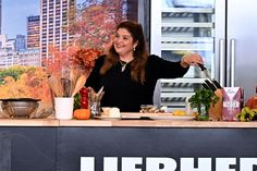 a woman standing in front of a kitchen counter with vegetables and fruit on the counter