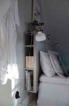 a white bed sitting under a window next to a shelf filled with pillows and blankets