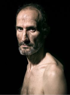 an older man with no shirt on posing for a photo in front of a black background