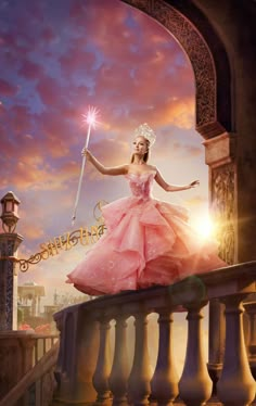 a beautiful woman in a pink dress holding a wand and standing on a balcony railing