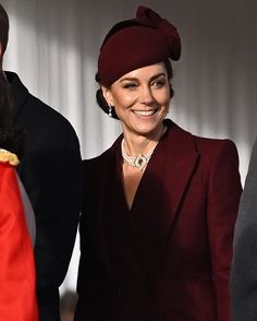 a woman in a red suit and hat smiles as she stands next to a man