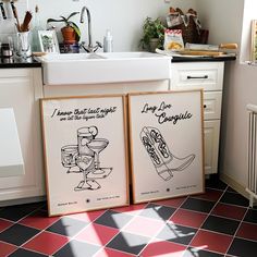 two framed posters sitting on top of a kitchen floor next to a sink and stove