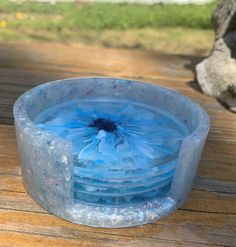 there is a plastic bowl with blue flowers in it on the wooden table outside by some rocks