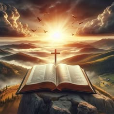 an open book sitting on top of a rock with a cross in the sky above it