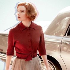 a woman standing in front of a car wearing a red shirt and skirt with a bow